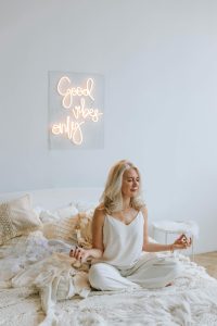 ine Frau meditiert in einem hellen und gemütlichen Raum mit dem leuchtenden Schriftzug „Good vibes only“. Das Bild verdeutlicht, wie wichtig Achtsamkeit und Meditation zur Stressbewältigung bei CMD sind.