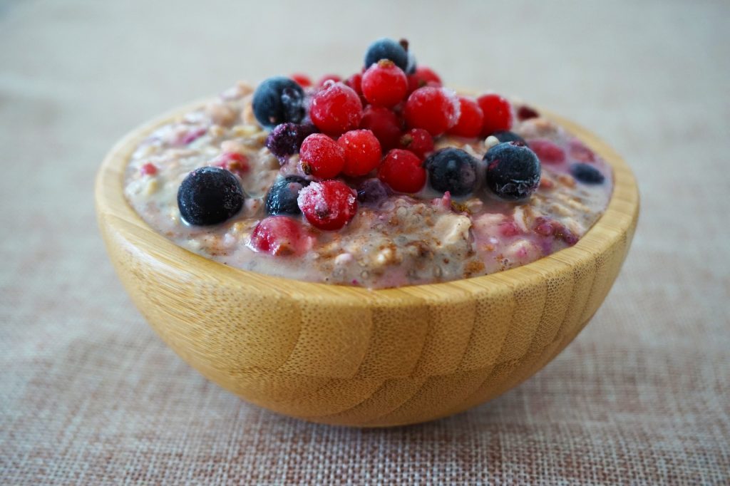 Eine Holzschale mit Haferbrei, garniert mit frischen Beeren wie Blaubeeren, Himbeeren und Johannisbeeren – ideal als weiche, nährstoffreiche Mahlzeit für CMD-Patienten. Keywords: Haferbrei, Beeren, Ernährung bei CMD.