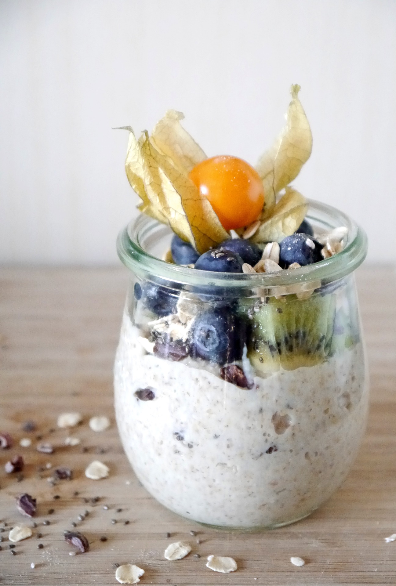 Ein Glas mit Overnight Oats, dekoriert mit Kiwi, Blaubeeren und einer Physalis – eine leicht kaubare, entzündungshemmende Mahlzeit für eine CMD-freundliche Ernährung. Keywords: Overnight Oats, entzündungshemmende Lebensmittel, CMD-Ernährung.