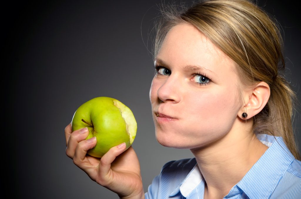 Nahaufnahme einer Frau, die in einen grünen Apfel beißt – Darstellung der Funktion des Kausystems und möglicher Zusammenhänge mit CMD (Craniomandibuläre Dysfunktion).