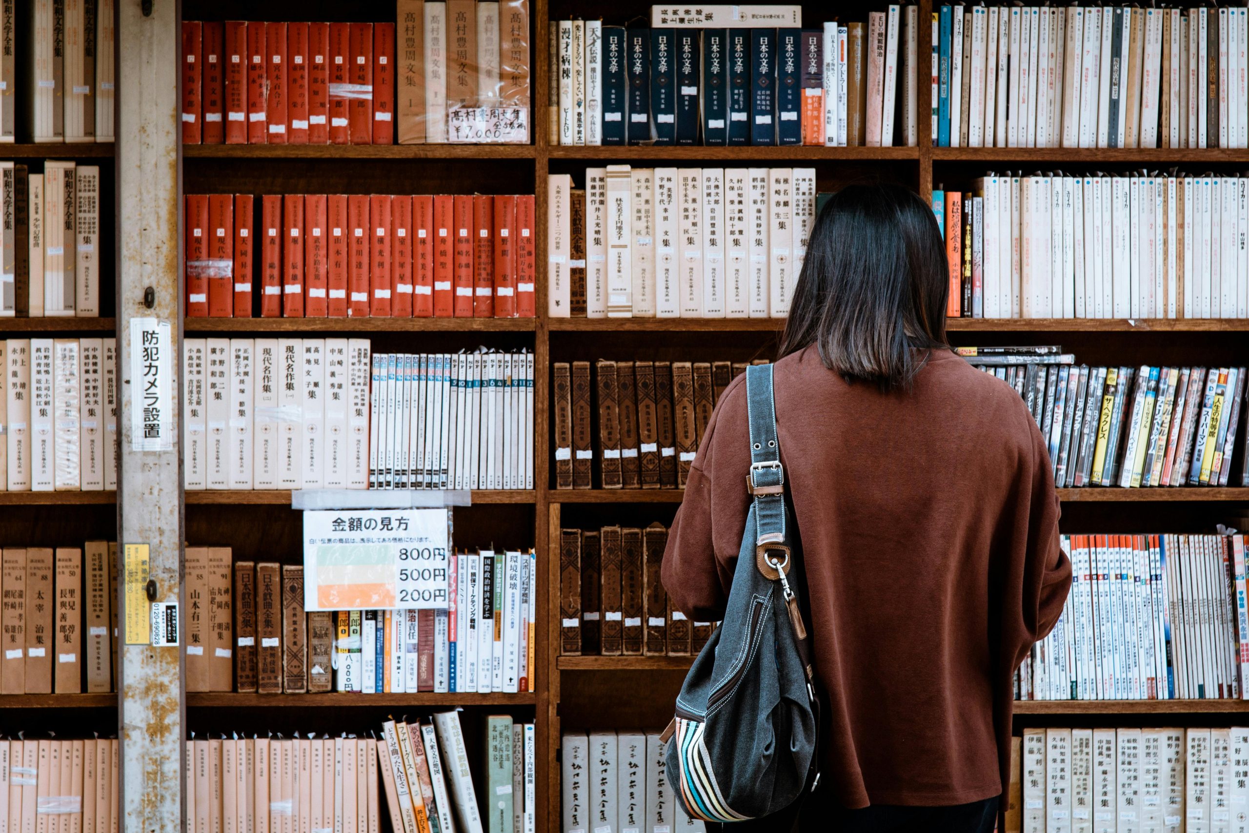 Eine Frau steht vor einem Regal voller Bücher und recherchiert Informationen – ein Sinnbild für die Bedeutung von Wissensaneignung im Rahmen der CMD-Therapie.