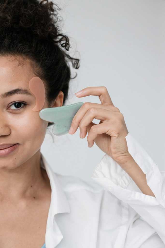 Frau hält einen Gua-Sha-Stein an ihre Gesichtsmuskulatur und massiert sanft die Wangenpartie. Diese Technik wird genutzt, um Muskelverspannungen im Gesicht zu lösen und die Durchblutung zu fördern – eine einfache Selbsthilfemaßnahme für CMD-Patienten.