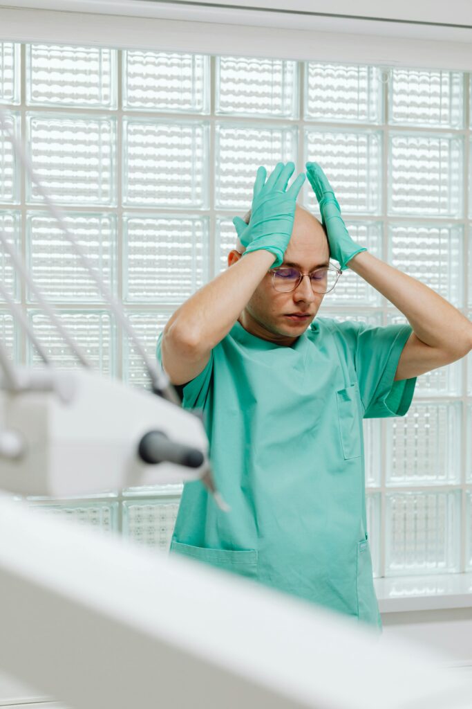 Ein gestresster Arzt hält sich mit Handschuhen den Kopf in einem klinischen Umfeld. Dieses Bild symbolisiert die Belastung durch chronische Schmerzen und die psychischen Auswirkungen von CMD, die oft mit Antidepressiva behandelt werden können.