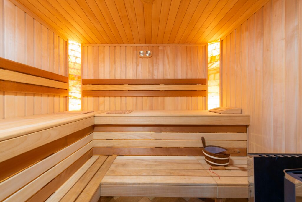 Eine gemütliche Sauna mit Holzverkleidung, die angenehme Wärme bietet. Wärmetherapie, wie sie durch Saunaaufenthalte erreicht wird, unterstützt die Regeneration von Muskeln und Gelenken bei CMD-Beschwerden.