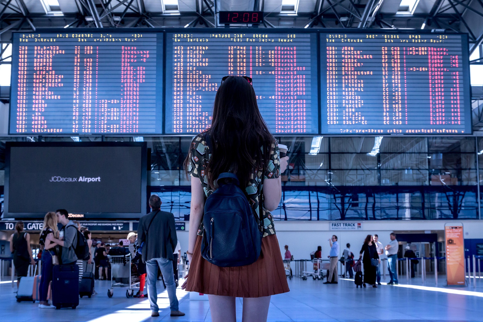 Eine Frau steht in einem belebten Flughafen vor einer großen Abflugtafel, einen Rucksack auf dem Rücken. Perfekt für Artikel über Reisen mit CMD und die Vorbereitung auf lange Strecken.