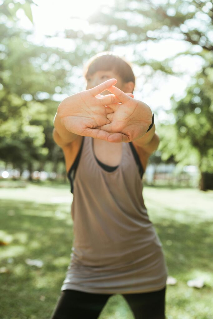 Die Übung zeigt eine Person in einer ruhigen, grünen Umgebung, die ihre Arme sanft dehnt. Das einfallende Sonnenlicht schafft eine entspannte Atmosphäre, die die beruhigende Wirkung von Tai Chi unterstreicht. Diese Bewegung fördert nicht nur die Durchblutung, sondern hilft auch dabei, muskuläre Verspannungen zu lösen, die oft mit CMD einhergehen. Die Kombination aus Bewegung und Natur trägt zur mentalen Entspannung bei.