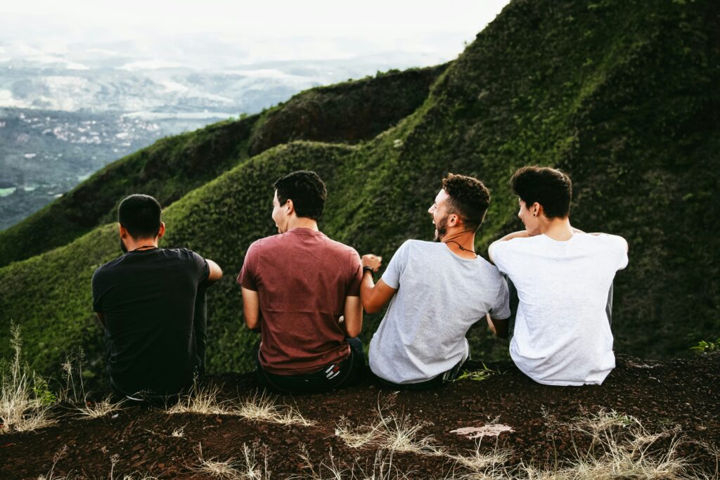 Vier junge Männer sitzen entspannt auf einem Berg – Symbolbild für männliche Gesundheit, Zusammenhalt und die oft verborgene Belastung durch Kieferprobleme.